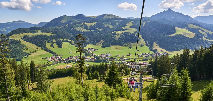 Sessellift über grüne Landschaft mit Bergen und Häusern im Hintergrund