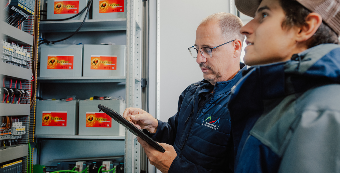 Zwei Männer betrachten Tablet vor Schaltschrank mit Batterien