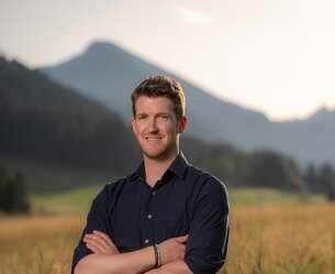 Mann mit verschränkten Armen vor Landschaft mit Berg