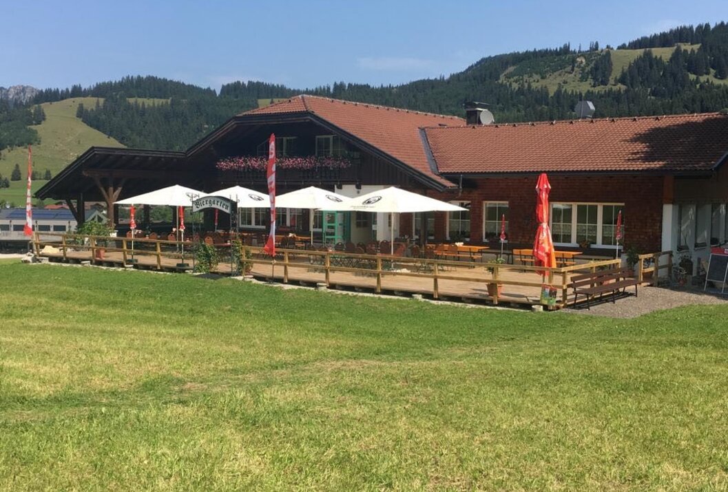 Traditionelles Gebäude mit Biergarten vor grüner Bergkulisse